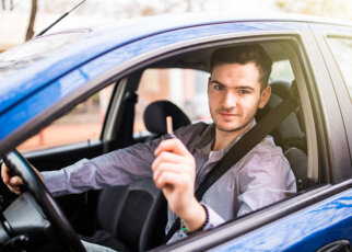 Young handsome man driving his new car, holding out keys