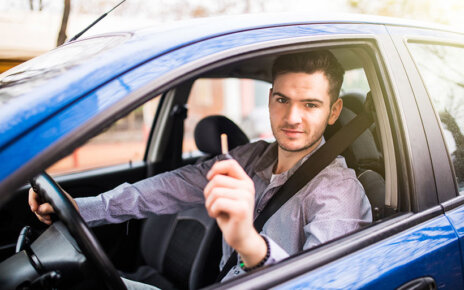 Young handsome man driving his new car, holding out keys